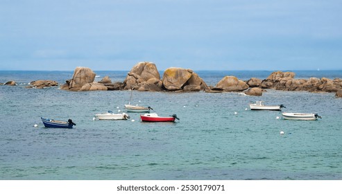 Small boats anchored near large rocks in Brittany in a calm sea under a cloudy sky. - Powered by Shutterstock