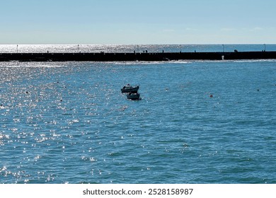 Small boats float on a calm sea with the sun reflecting off the water near a pier. Figures walk along the pier in the distance. The photo captures a peaceful maritime scene near Cádiz.
 - Powered by Shutterstock