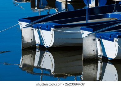 Small boats are lined up at a dock, their reflections shimmering in clear water. The tranquil scene captures the essence of a sunny day, inviting relaxation and observation of nature.