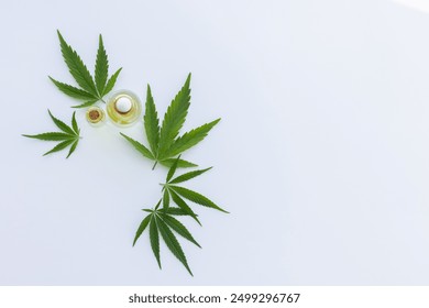 Small bottles with cannabis oil between fresh cannabis leaves. Top view. On a white background with copy space.