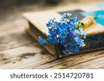 Small bouquet of blue forget-me-not flowers with old book on the wooden background. Selective focus. Shallow depth of field.