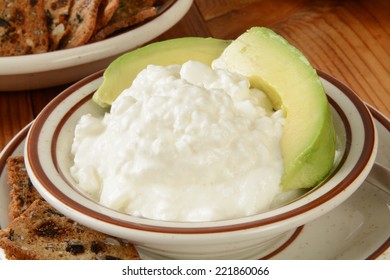 A Small Bowl Of Cottage Cheese With Avocado And Crackers