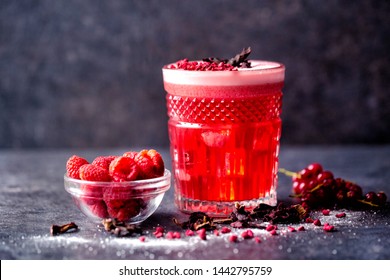 Small bowl of raspberries, glass of delicious cocktail and some cranberries on a dark background