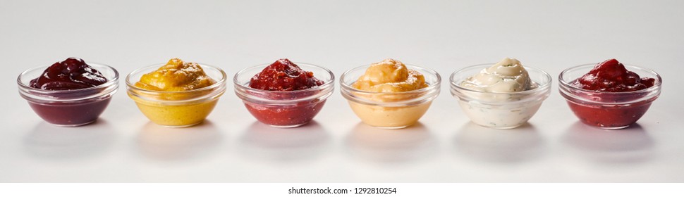 Small Bowls Of Assorted Sauces, Dips, Marinades And Dressings On White With Reflections In A Panorama Banner