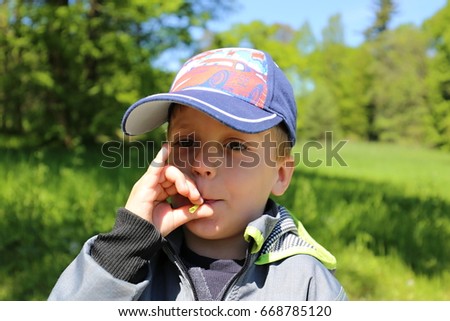 Small boy in baseball cap blowing to the dandelion footstalk