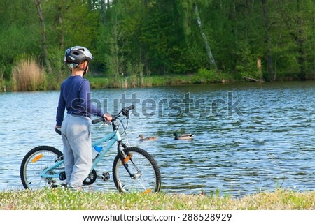 Small boy, bikerider in sport helmet  on the beach. Pair of ducks on the water level.
