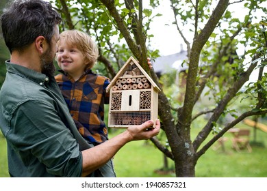 Small boy with father holding bug and insect hotel in garden, sustainable lifestyle.