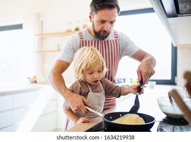 A small boy with father indoors in kitchen making pancakes.