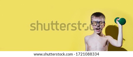 Small boy in glasses holding dumbbell in hand. Child's face feeling very heavy. Funny sport concept. Banner and panoramic edition.