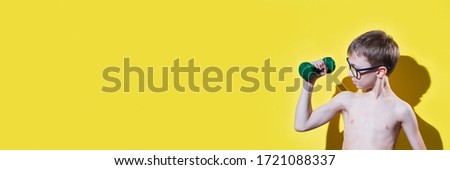 Small boy in glasses holding dumbbell in hand. Sport and fitness concept. Banner edition.	