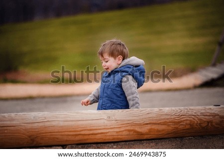 A small boy laughs with delight while playing on a wooden structure at a playground, the embodiment of childhood merriment and unbridled happiness