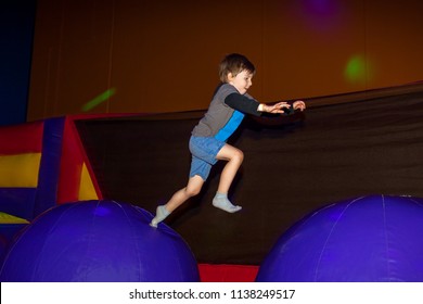 A small boy leaps from one inflatable obstacle to another in an indoor play place with the lights out.  The picture was taken mid jump. - Powered by Shutterstock