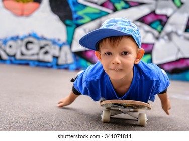 Small boy lying on his skateboard using his hands to propel himself along in front of a colorful painted graffiti wall, close up with him facing the camera - Powered by Shutterstock