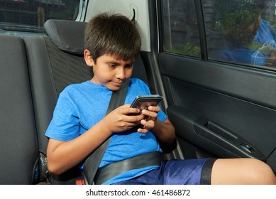 Small Boy With Phone On Back Seat Of Car