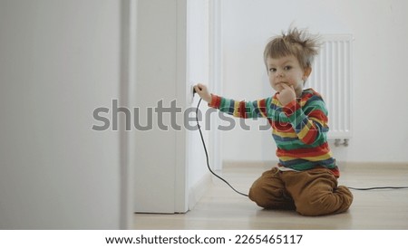Small boy playing with electrical plug into the wall socket, unsafe activity
