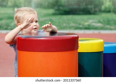 Small boy  plays a colorful drums in public playground. Happy child hiding behind a line of drums. Feel the music everywhere