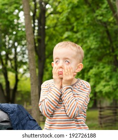 Small boy pulling a funny face distorting his features with his hands as he amuses himself outdoors in a leafy green park