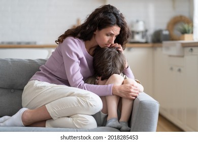 Small Boy Receiving Love, Protection And Support From Loving Mom Cuddling Little Son Offended Child Cry On Sofa. Caring Mother Consoling Kid With Tender Embraces. Worried Parent Hug Upset Preschooler