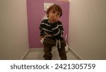 Small boy seated at bathroom toilet and picking nose