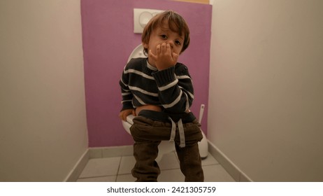 Niño pequeño sentado en el inodoro del baño y en la nariz de escopeta