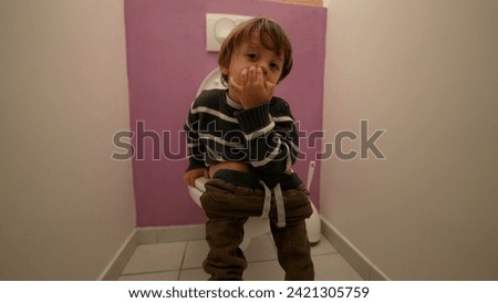 Small boy seated at bathroom toilet and picking nose