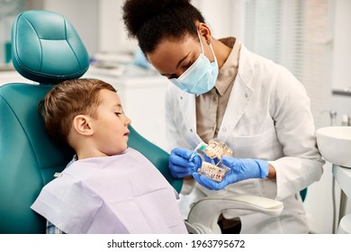 Small boy sitting in dentist's chair and learning how to brush teeth properly.