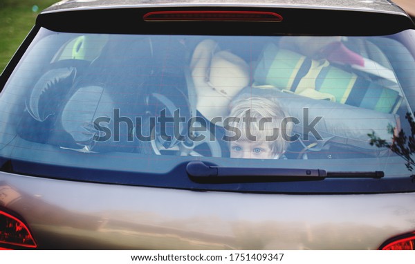 Small boy sitting in loaded car boot with closed\
door, local trip concept.