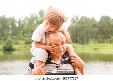 Small boy is sitting on his grandfather On Walk in the summer outdoors. Concept of friendly family.
