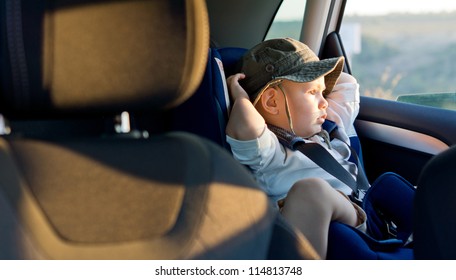 Small Boy Sitting Strapped Into A Child Seat In The Rear Of A Car Staring Out Of The Window