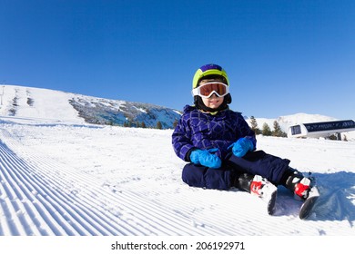 Small Boy In Ski Mask Sitting On The Snow