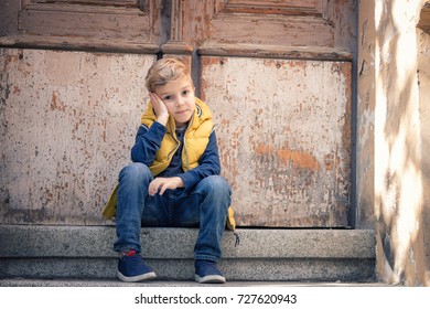 Small Boy Thinking While Sitting In Front Of A Door And Waiting For Someone. Bored Child Relaxing On Stairs. 