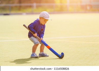 Small boy training playing field hockey with stick on the field
