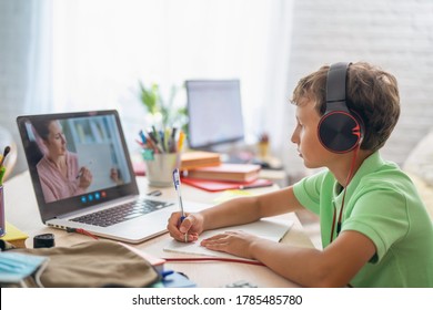 small boy uses laptop to make video call with his teacher. screen shows an online lecture with teacher explaining subject from class. E-Education Distance Learning, Home Schooling. Side view.