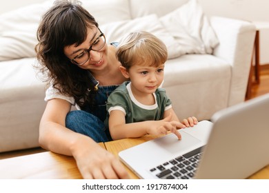 Small Boy Using Laptop While Sitting With Mother At Home. Kid Learning To Use Laptop With His Mother In Living Room.