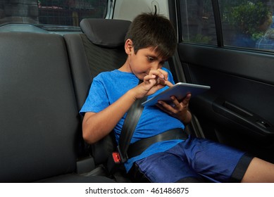 Small Boy Using Tablet On Back Seat Of Car