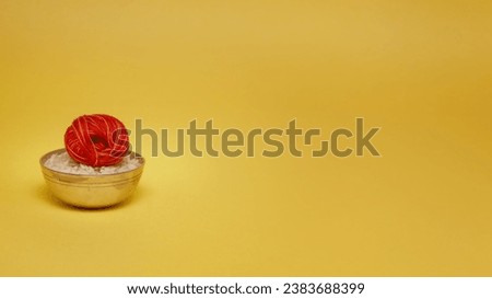 Small brass bowl with rice and kalawa (pooja thread). Hindu pooja object over a yellow background.