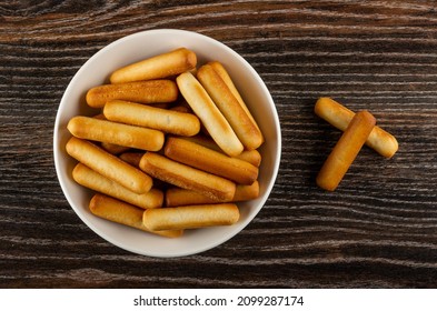 Small bread sticks in white glass plate, breadsticks on dark wooden table. Top view