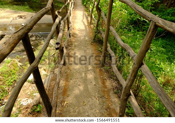 a small bridge by the river in the countryside.\
the handle and divider on this bridge are made of wood. scrub\
growing around rivers and bridges. in the tropics bushes of green\
foliage grow easily.