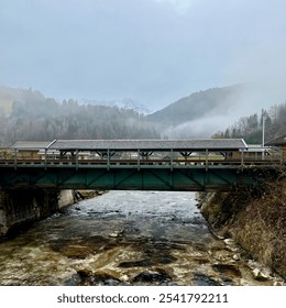 A small bridge at Pachtnach spans a clear river with misty mountain views in the background, creating a serene, atmospheric scene en route to Partnachklamm Gorge, Germany. - Powered by Shutterstock