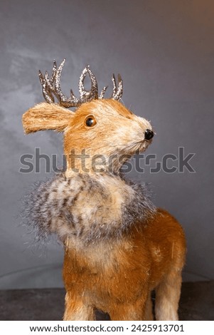 Small brown deer figurine with silver antlers and black nose and hooves, placed on a gray surface and facing the camera.