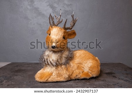 Small brown deer figurine with silver antlers and black nose and hooves, placed on a gray surface and facing the camera.