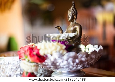 A small Buddha image is placed on a pedestal and a flower garland is placed on top of the Buddha image. Concept of Buddhism in Thailand Paying homage to monks during Songkran Festival