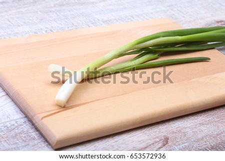 Small bundle of washed fresh green onions with long stems and tiny roots on wood table.