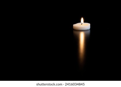 Small burning candle and its reflection on a black table with empty space
