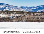 Small bush plane aircraft takes off from frozen Lake Laberge in Yukon Territory winter wilderness landscape of boreal forest taiga hills, YT,  Canada