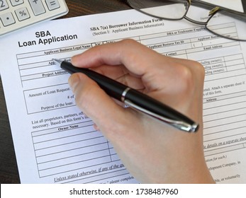 A Small Business Administration Aka SBA Loan Application Form, Issued By The U.S.A. Government, Is Shown Up Close Just Before Being Filled Out By A Female Hand With An Ink Pen.