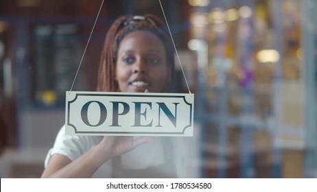 Small business african female owner smiling while turning sign for opening of cafe. Happy afro-american waitress in apron turning sign on door opening restaurant in morning. - Powered by Shutterstock