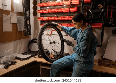 Small business bike repair. Young caucasian woman wearing uniform, uses mobile phone technology, takes notes in bicycle workshop. Copy space - Powered by Shutterstock