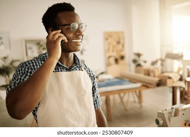 Small business, black man and happy on phone call as tailor for communication and connection with client. Male person, fashion designer and smile or satisfied with clothes order at textile workshop - Powered by Shutterstock