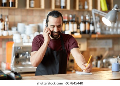 Small Business, Communication, People And Service Concept - Happy Man Or Waiter In Apron Calling On Smartphone At Bar Or Coffee Shop